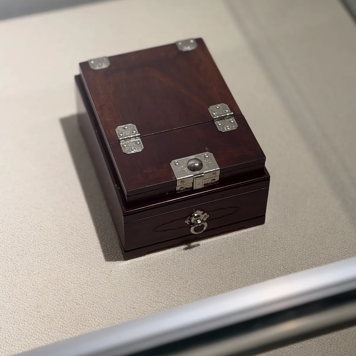 A small dark wooden box with silver hinges and a drawer
